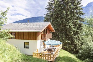 A two-story wooden cabin with a deck and outdoor seating area, surrounded by trees and mountains. - Cabin in Annaberg with swimming pool (Annaberg)
