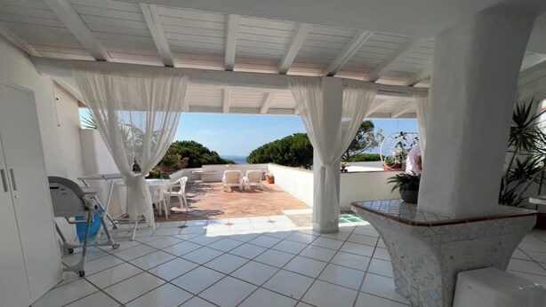 Ein überdachter Patio-Bereich mit Fliesenboden, weißer Möbel und Blick auf den Ozean.