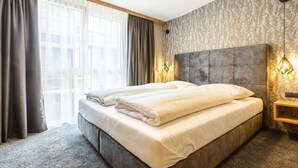 Habitació d'hotel amb un llit gran, un capçal, una tauleta de nit i una finestra amb cortines.