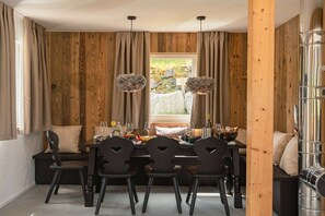 Un coin repas avec un mur en bois, une table dressée pour quatre personnes et une vue sur un jardin par la fenêtre.
