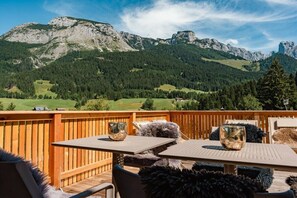 A wooden deck with a table and chairs, overlooking a mountainous landscape. - Cabin in Annaberg with swimming pool (Annaberg)