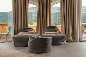 Une pièce avec deux fauteuils poire et des poufs, une terrasse en bois et une vue sur les montagnes.