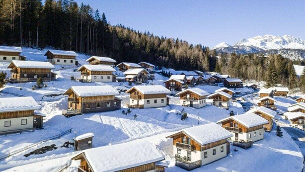 A snow-covered village with wooden cabins, a forested hillside, and snow-capped mountains in the background. - Cabin in Annaberg with swimming pool (Annaberg)