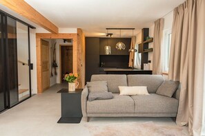 Un salon moderne avec un canapé gris, une petite table d’appoint sur laquelle est posé un vase, et une poutre en bois au plafond.