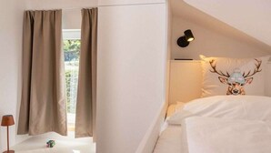 A bedroom with a bed, curtains, a lamp, a wall-mounted light, and a pillow with a deer design. - Cabin in Annaberg with swimming pool (Annaberg)
