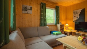 Interior de una cabaña de madera con un sofá, un televisor y una mesa con fruta.