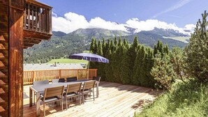 A wooden deck with a table and chairs, overlooking a mountainous landscape. - Cabin in Annaberg with swimming pool (Annaberg)