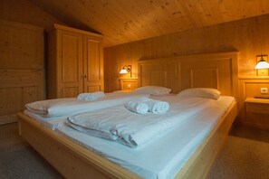 A double bed with white linens and towels, wooden walls, and two bedside lamps. - Cabin in Annaberg with swimming pool (Annaberg)