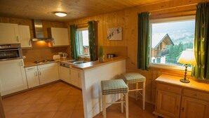 Una cocina con armarios de madera, estufa, pileta y dos taburetes.