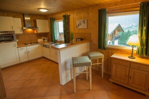 Een keuken met houten kastjes, een fornuis, een spoelbak en twee krukken.