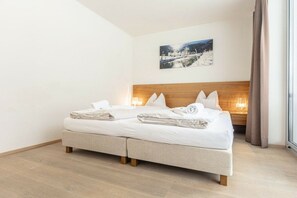 Cama de casal com cabeceira de madeira, roupa de cama branca e mesa de cabeceira com abajur.
