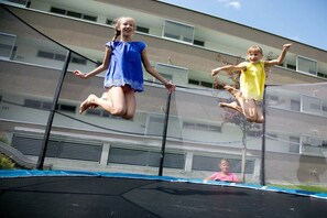 Two children jumping on a trampoline with a building in the background. - Apartment in Radstadt with swimming pool (Radstadt)