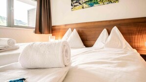 Habitació d'hotel amb un llit ben fet, una tovallola blanca arremolinada i un objecte blau petit sobre el llit.