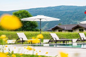 A pool area with lounge chairs and umbrellas, surrounded by a grassy landscape and a mountain in the background. - Apartment in Radstadt with swimming pool (Radstadt)