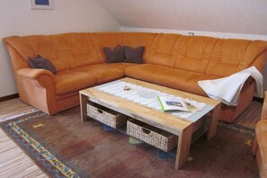 A living room with a sectional sofa, a coffee table with a lace tablecloth, and a patterned rug. - Holiday apartment Brigitte DG (Flörsbachtal)