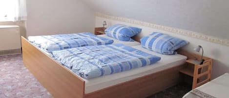 Un lit simple avec un cadre en bois et une couverture à carreaux bleus et blancs. Il y a une table de chevet avec une lampe dessus.