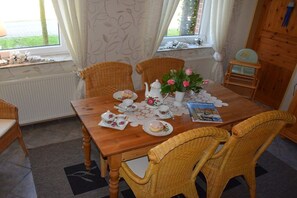Ein Esstisch ist gedeckt mit Teetassen, Untertassen und einer Teekanne, umgeben von Korbstühlen.