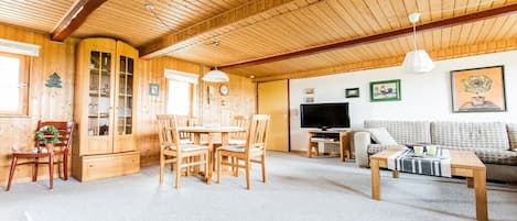 A wooden interior with a dining area, a sofa, and a television.