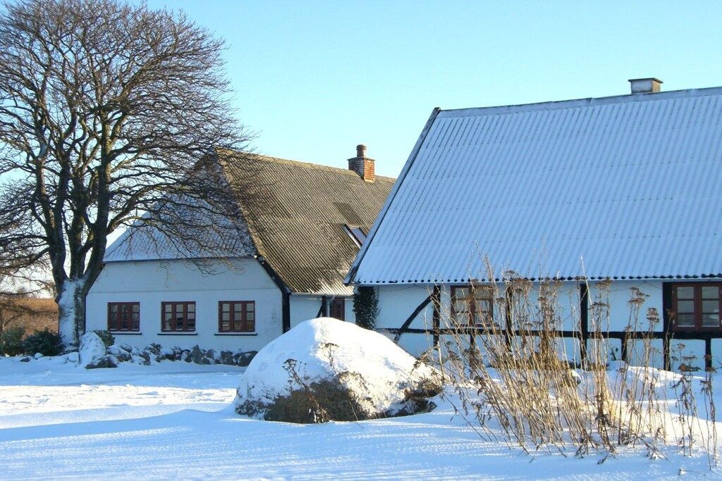 Een traditioneel gebouw met een schuin dak, een grote rots op de voorgrond en een besneeerd landschap.