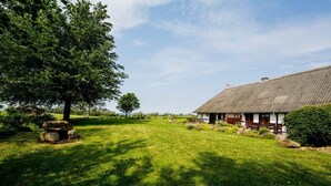 A traditional house with a thatched roof, surrounded by a well-maintained lawn and a large tree. - Nydamsgaard "hus mælkebøtte" (Faaborg \/ Bojden)