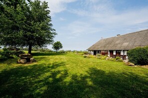 A traditional house with a thatched roof, surrounded by a well-maintained lawn and a large tree. - Nydamsgaard "hus mælkebøtte" (Faaborg \/ Bojden)