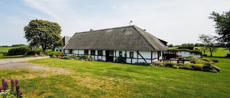 A traditional half-timbered house with a sloped roof, surrounded by a well-maintained lawn and a large tree.