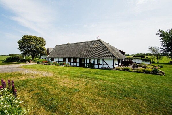 A traditional half-timbered house with a sloped roof, surrounded by a well-maintained lawn and a large tree. - Nydamsgaard "hus mælkebøtte" (Faaborg \/ Bojden)