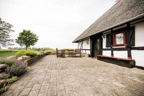 A building with a stone-paved patio, wooden furniture, and a view of a green landscape. - Nydamsgaard "hus mælkebøtte" (Faaborg \/ Bojden)