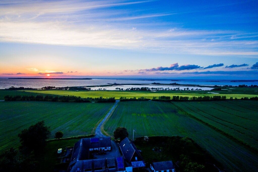 Un paysage rural avec des champs, une route et une étendue d’eau au coucher du soleil.