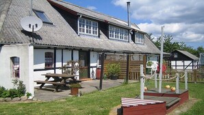 A traditional building with a sloped roof, a wooden bench, and a picnic table. - Nydamsgaard "hus mælkebøtte" (Faaborg \/ Bojden)