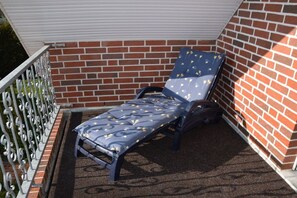 Een blauwe loungestoel met een gekleurd kussen op een balkon met een bakstenen muur en metalen hekwerk.