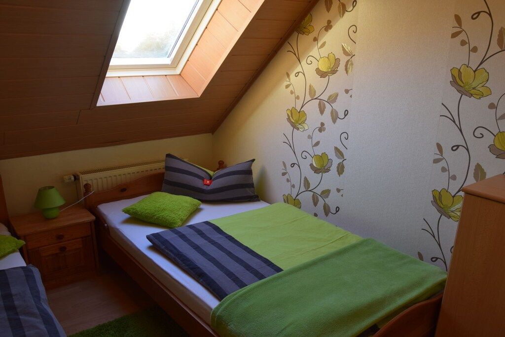 A bedroom with a skylight, a bed with green and gray bedding, a nightstand with a lamp, and floral wallpaper.