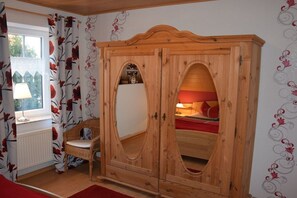Een kamer met een houten garderobe, een rieten stoel en een bed met rode beddengoed.