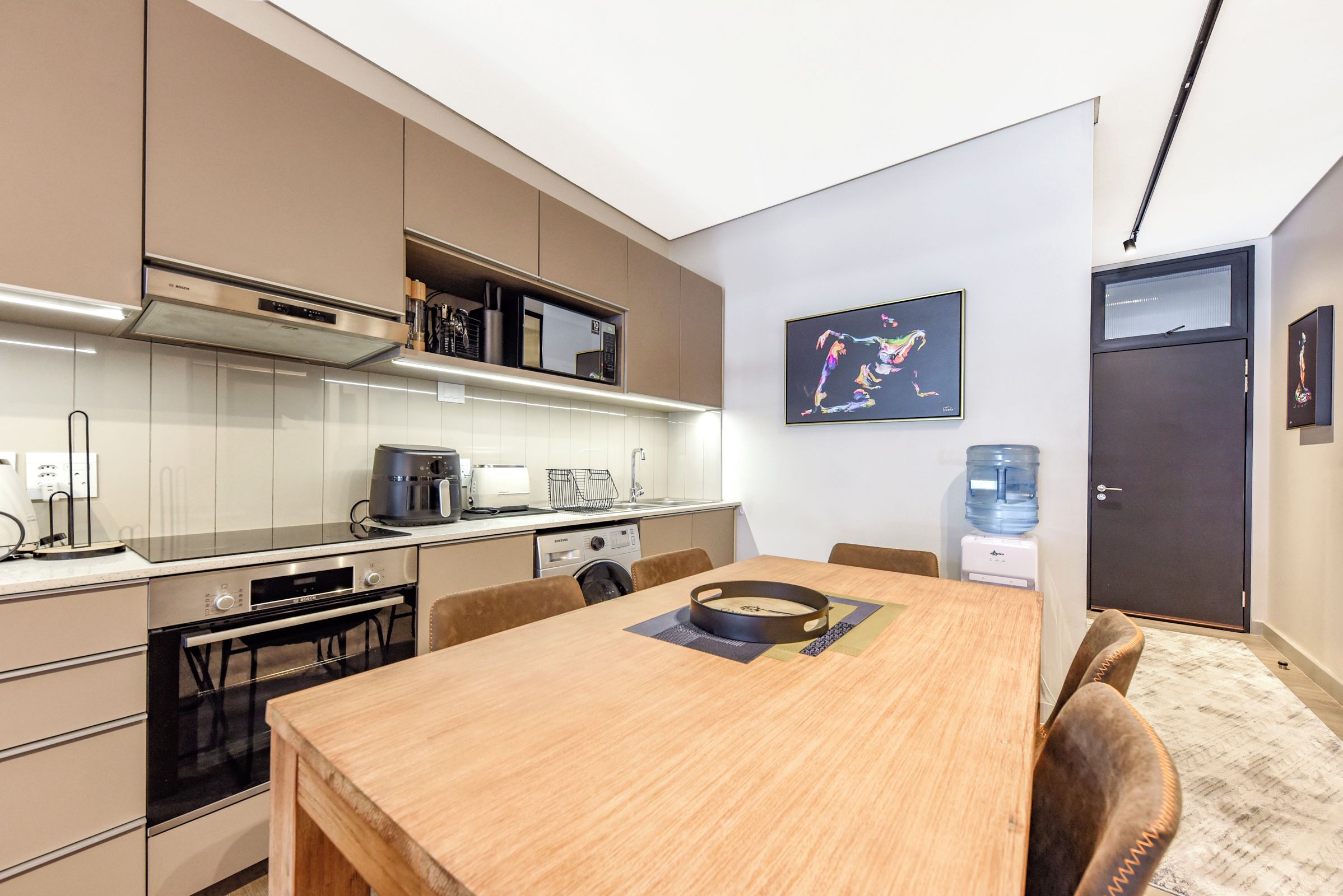 Una cocina moderna con electrodomésticos Bosch, un comedor con mesa, sillas y dispensador de agua.