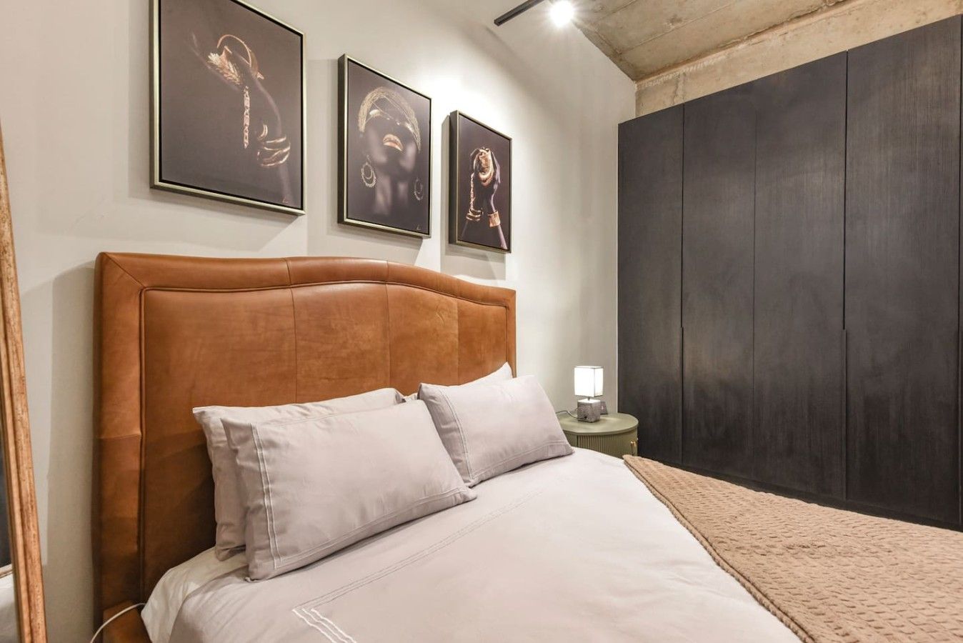 A bedroom with a large bed, a wooden headboard, a nightstand with a lamp, and a dark wardrobe.