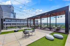 Un patio al aire libre con zona de comedor, asientos y vistas a un paisaje urbano.
