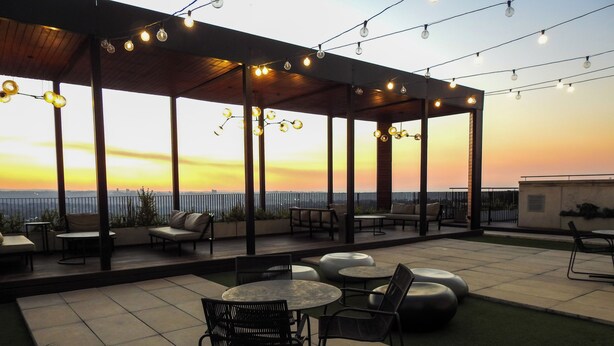 Un espacio al aire libre con mesas y sillas, una zona cubierta con luces colgantes y vistas al atardecer.