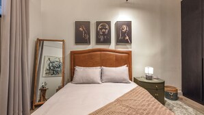 Un dormitorio con una cama grande, una mesita de noche con una lámpara y tres cuadros en la pared.