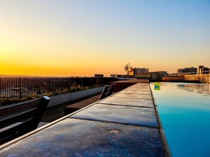 Ein Poolbereich auf dem Dach mit Blick auf die Skyline der Stadt bei Sonnenuntergang.