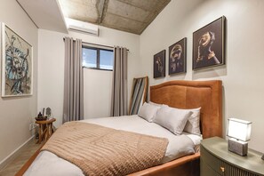 Un dormitorio con una cama, una mesita de noche, una lámpara y obras de arte en las paredes.