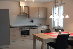 A modern kitchen with stainless steel appliances, wooden cabinets, and a dining area with a table and chairs. - Holiday apartment with 1 bedroom (Vogtsburg-Oberbergen)
