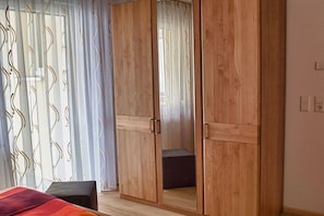A room with a bed, a wooden wardrobe, and a window with curtains. - Holiday apartment with 1 bedroom (Vogtsburg-Oberbergen)