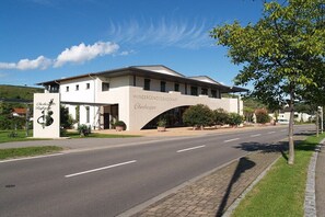 A building with a sign reading 'Winzergenossenschaft' and 'Oberbergen.' It has a modern architectural style with a flat roof and a large arched entrance. - Holiday apartment with 1 bedroom (Vogtsburg-Oberbergen)