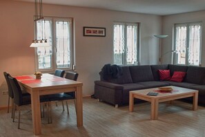A living room with a sofa, a coffee table, a dining table with chairs, and a pendant light. - Holiday apartment with 1 bedroom (Vogtsburg-Oberbergen)