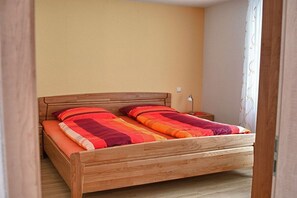 A wooden bed with a headboard, a bedside table, and a wall socket. - Holiday apartment with 1 bedroom (Vogtsburg-Oberbergen)