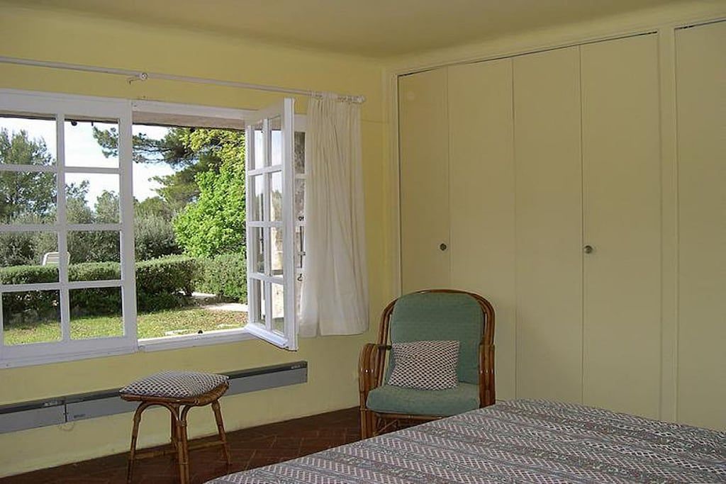 Een kamer met een bed, een stoel, een raam met gordijnen en een kledingkast.