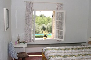 Ein Schlafzimmer mit Bett, Schreibtisch mit Lampe und einem Fenster mit Vorhängen.