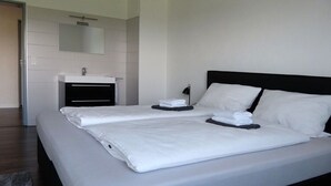 Quarto de hotel moderno com uma cama grande, uma mesinha de cabeceira, um espelho e banheiro com pia.