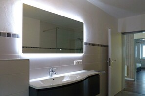 A modern bathroom with a large mirror, a white sink, and a shower area. - City view Winterberg (Winterberg)