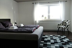 Une chambre à coucher avec un lit, une chaise, une fenêtre avec des rideaux et un radiateur.